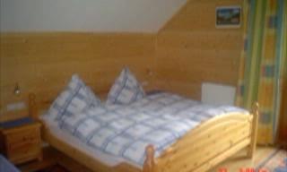 A simple bedroom with a double bed and wooden panels. The room is bright and inviting, with a nightstand and colorful curtains.