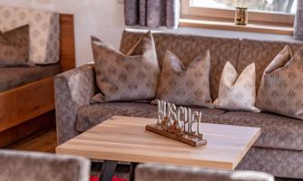 A cozy living room with a beige sofa and decorative cushions. On the table lies a wooden sign with the word "Wuschel".