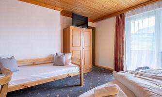 A bright bedroom with a wooden ceiling and a single bed as well as a double bed. A wardrobe and a television are also available.
