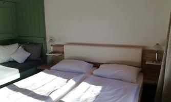 A cozy bedroom with two beds and a seating area. The walls are painted in friendly colors, creating an inviting atmosphere.