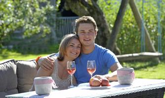 A cheerful couple is sitting in the garden at a table. They are enjoying rosé wine and the sunny atmosphere.