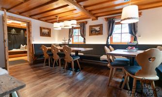 A cozy dining area with wooden tables and chairs. The room is brightly lit and has a warm, inviting atmosphere.