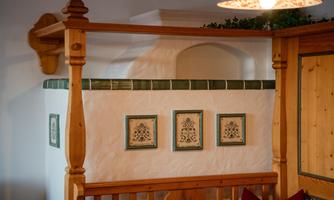 A cozy interior with a wood structure. Three decorative pictures hang on the wall, and a tiled stove is visible.