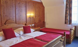 A cozy bedroom with a double bed and a single bed. The walls are lined with wood and there is warm lighting.
