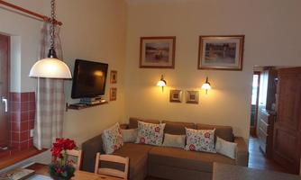 A cozy living room with a sofa and decorative pillows. Pictures are hanging on the wall, and there is a television as well as a dining table.