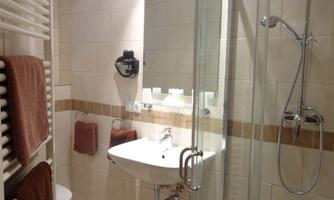 A modern bathroom with a glass shower and a sink. Towels hang on the wall, and the walls are light tiled.