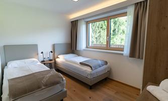 A bright bedroom with two single beds and a large window. The walls are painted in neutral tones, creating a calming atmosphere.