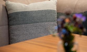 A cozy sofa with a striped cushion and a wooden table in the foreground. On the table, there is a vase with fresh flowers.