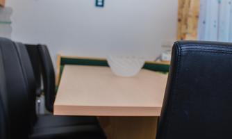 A cozy table with black chairs and a bowl on the tabletop. The wall in the background is bright and has a window with curtains.