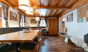 A cozy dining area with a large wooden table and several chairs. The walls are decorated with wood paneling and decorative pictures.