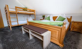 A cozy room with a double bed and a bunk bed. The furniture is made of light wood and there are green cushions.