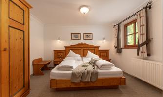 A cozy bedroom with a large double bed and wooden furniture. The room has a window overlooking the outdoors and soft colors that create a relaxing atmosphere.