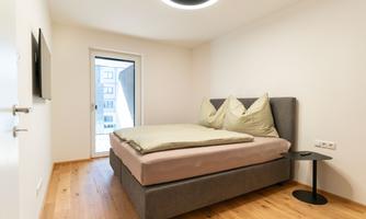 A modern bedroom with a large bed and bright walls. There is a small table next to the bed and a view of a balcony.