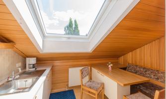 A cozy kitchen with wood paneling and a skylight. There are two chairs and a flower vase at the table.