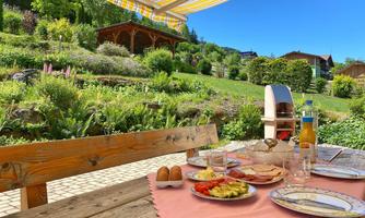 An idyllic garden with a set table, where a delicious breakfast awaits. In the background, green plants and a blue sky are visible.