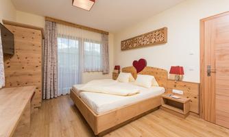 A cozy bedroom with a double bed, wooden details, and warm colors. Large windows let in plenty of light and create an inviting atmosphere.