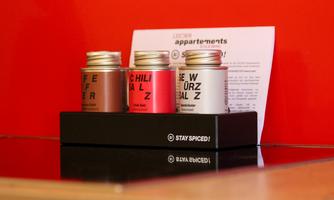 Three spice containers in different colors are on a black stand. In the background, a sheet of paper with information can be seen.