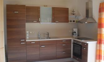 A modern kitchen with wooden fronts and a functional layout. It features a stove, a sink, and a refrigerator.