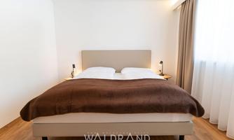 A modern bedroom with a double bed and soft colors. The windows let in plenty of daylight.