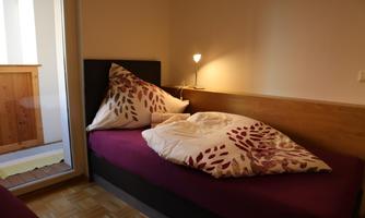 A cozy room with a single bed and a warm lamp. The cushions are adorned with a floral pattern.