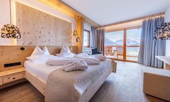 A modern and cozy bedroom with wooden furniture. Large windows offer a beautiful view of the mountains.