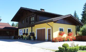 A charming half-timbered house with a yellow facade and a red roof. The garden is adorned with colorful flowers and well-maintained grass.