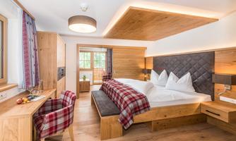 A modern hotel room with wooden decor and bright colors. There is a large bed, a small table, and plenty of daylight.