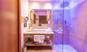 A modern bathroom with a glass shower and warm light. Fresh towels and toiletries are placed on the vanity.