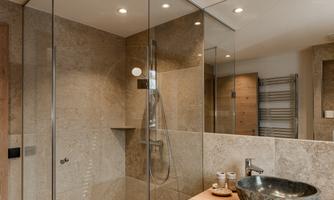 A modern bathroom with a glass enclosure and an elegant shower. The wooden washbasin top complements the stylish design.