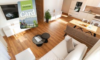 A modern living room with a bright decor and wooden flooring. On a table, there are round side tables, and there is a large window front that lets in plenty of light.