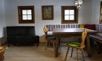 A cozy room with wooden windows and a large table.  
On the bench are colorful cushions, and the walls are painted light.