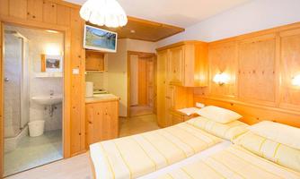 A cozy hotel room with two beds and warm wooden elements. There is a bathroom and a small TV in the room.