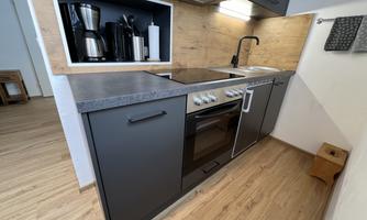 A modern kitchen featuring a combination of dark cabinets and wooden details. It is well-equipped with a stove, a sink, and coffee machines.