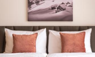 A stylish bedroom with a large window and two pillows in warm tones. On the bed lies a camera and a plant on a rustic fabric.