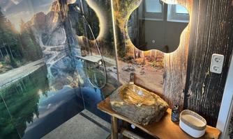 A modern shower with wall design that depicts a natural landscape. The room features a wooden wash basin and a petrified wooden sink that is 20 million years old.