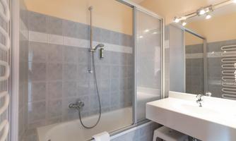 A modern bathroom with a shower and bathtub. The walls are tiled in light gray and there is a large mirror above the sink.