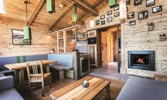 A cozy wooden house with an open living area. There is a dining table, a kitchen, and a fireplace that creates a warm atmosphere.