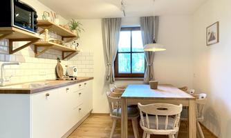A modern kitchen with a large dining table and bright colors. Shelves with dishes and plants give the space an inviting atmosphere.