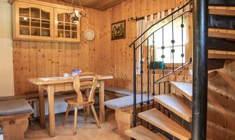 A cozy interior with wooden paneling and a table with chairs. The staircase in the background leads upstairs and creates an inviting atmosphere.