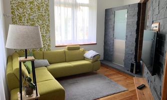 A modern living room with a light green sofa and a rug. The walls are partially designed with light and gray color tones.