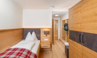 A cozy room with wooden cabinets and a single bed. The bright design and warm light create an inviting atmosphere.
