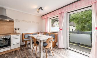 A modern kitchen with a dining table and wooden furniture. Large windows let in a lot of light and offer a view outside.