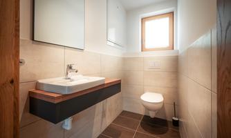 A modern bathroom with a floating sink and a toilet. The window provides natural light and a clear view outside.
