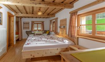 A cozy room with a wooden ceiling and two beds. Large windows let in plenty of daylight and provide a view of the greenery.