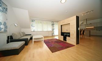A modern living room with a cozy couch and a table. The room is bright and has large windows with floral curtains.