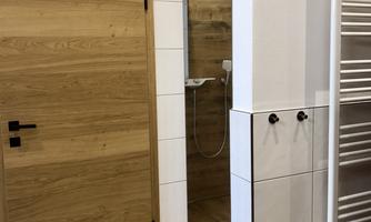 A modern bathroom with wood and tile accents. On display are a shower, a wooden sliding door, and a towel warmer.