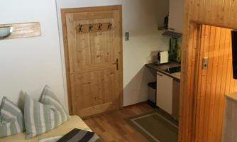 A cozy room with a bed and a kitchenette. The wood paneling and the floor give the space a warm atmosphere.