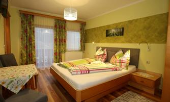 A cozy bedroom with a double bed, colorful cushions, and a small table. Large windows provide plenty of light and an inviting atmosphere.