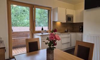 A modern kitchen with a dining table and a bouquet of flowers. Large windows offer a view of nature outside.