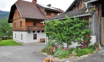 A picturesque wooden village house with a beautiful garden. In the foreground, a dog is passing by.